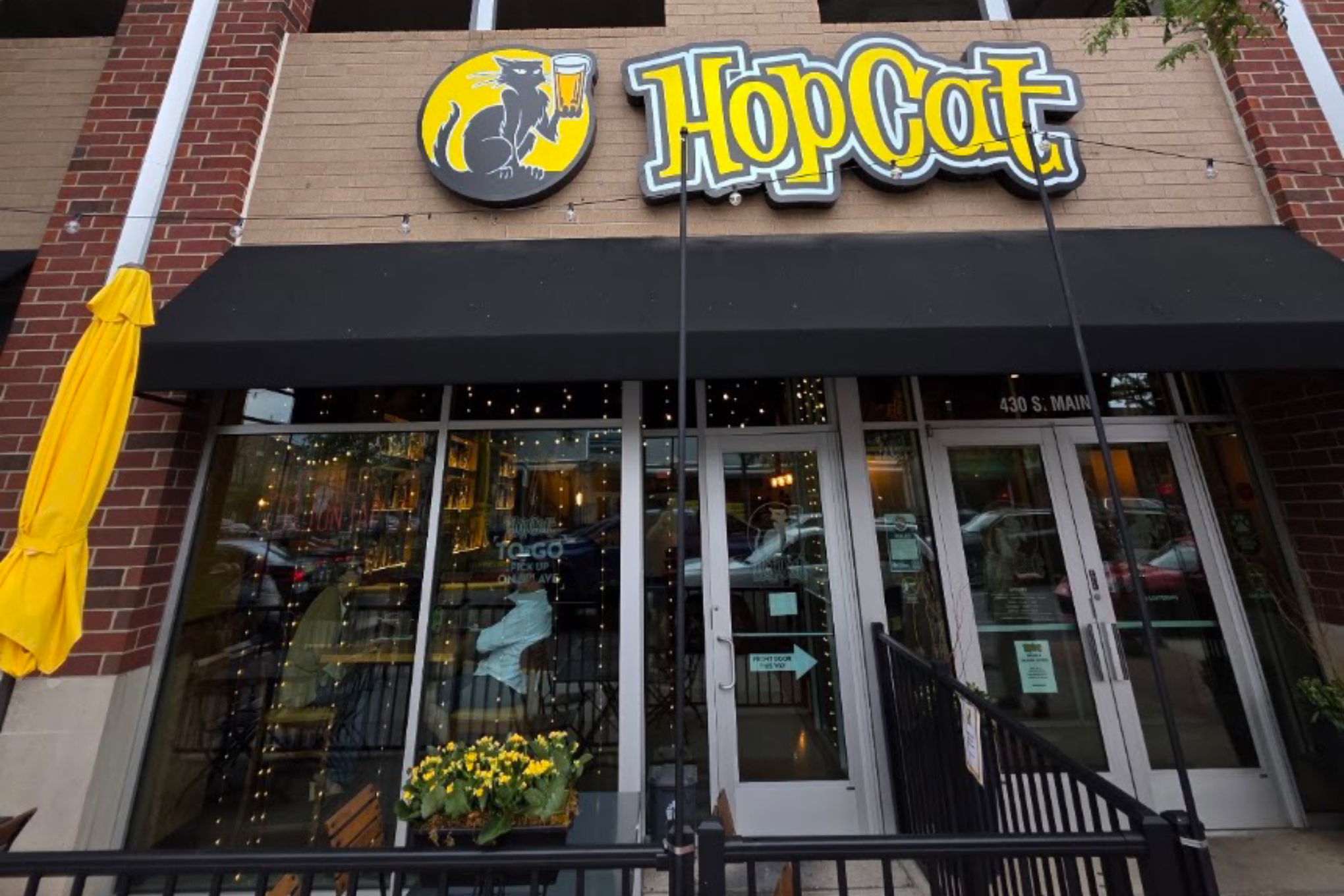 HopCat restaurant storefront with a yellow-and-gray sign featuring a cat and a beer mug above glass doors.